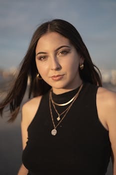 Portrait of a young woman with jewelry, black crop top, and windblown hair at sunset.
